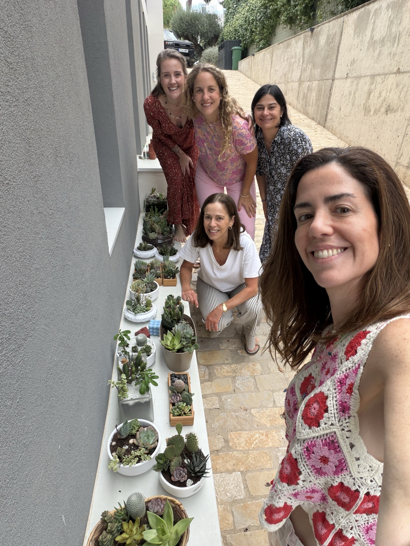 Cinco mujeres sonríen junto a una fila de macetas con suculentas